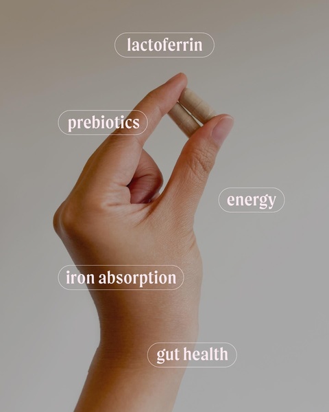 A clean, studio-lit image of a hand holding supplement capsules, featuring floating text labels that highlight core product benefits and ingredients.